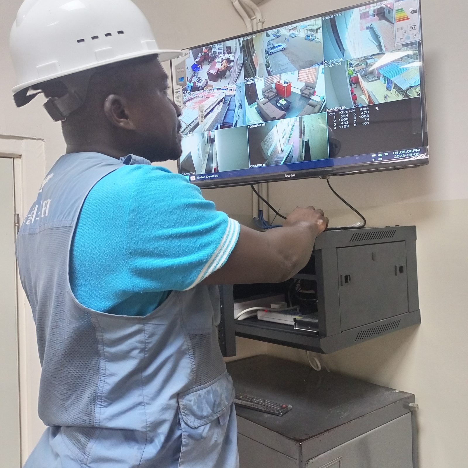 AerixSys technician mounting a network cabinet beneath a live CCTV monitoring display